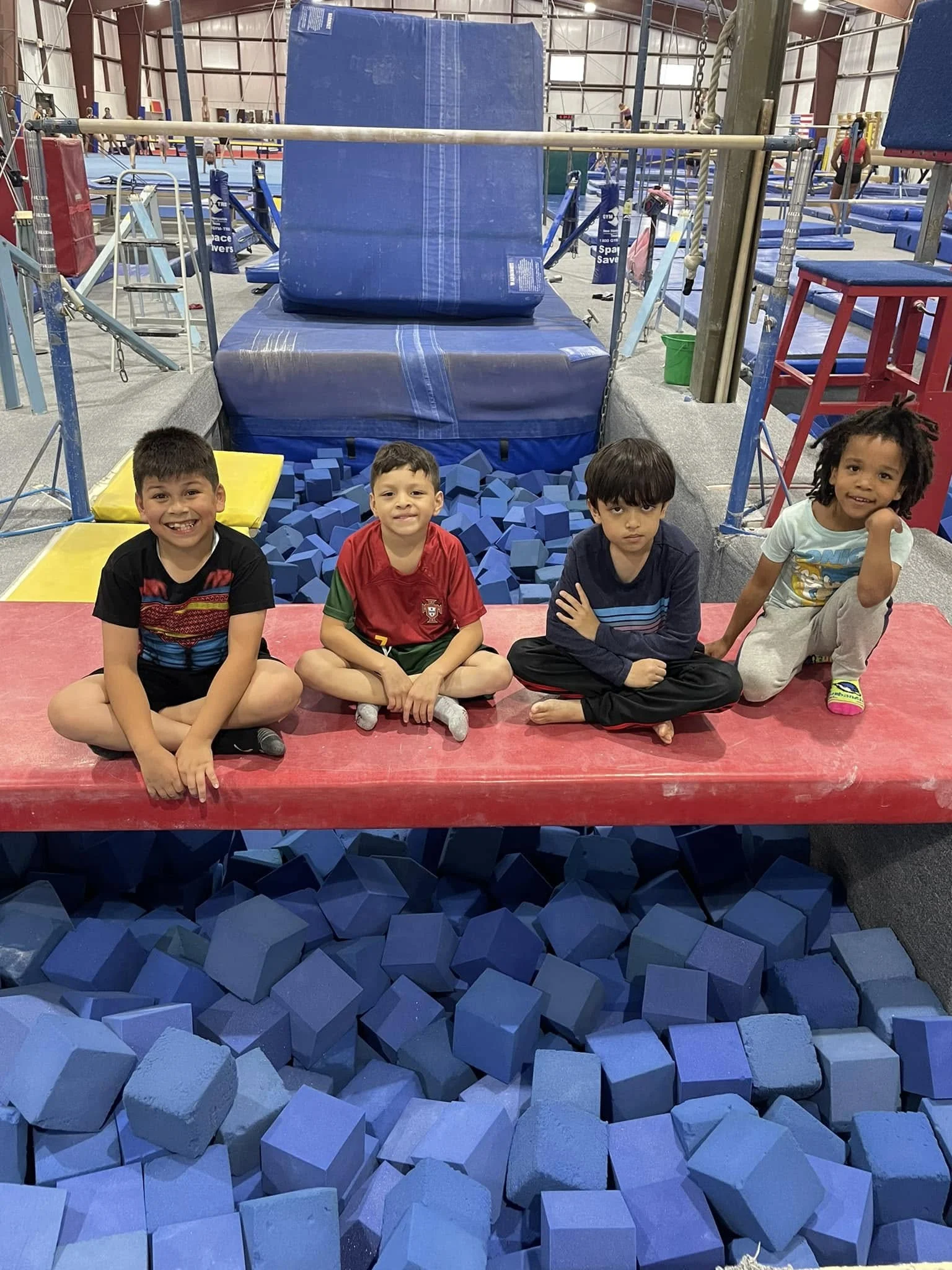 Four boys sitting on a padded beam above the foam pit at Scamps
