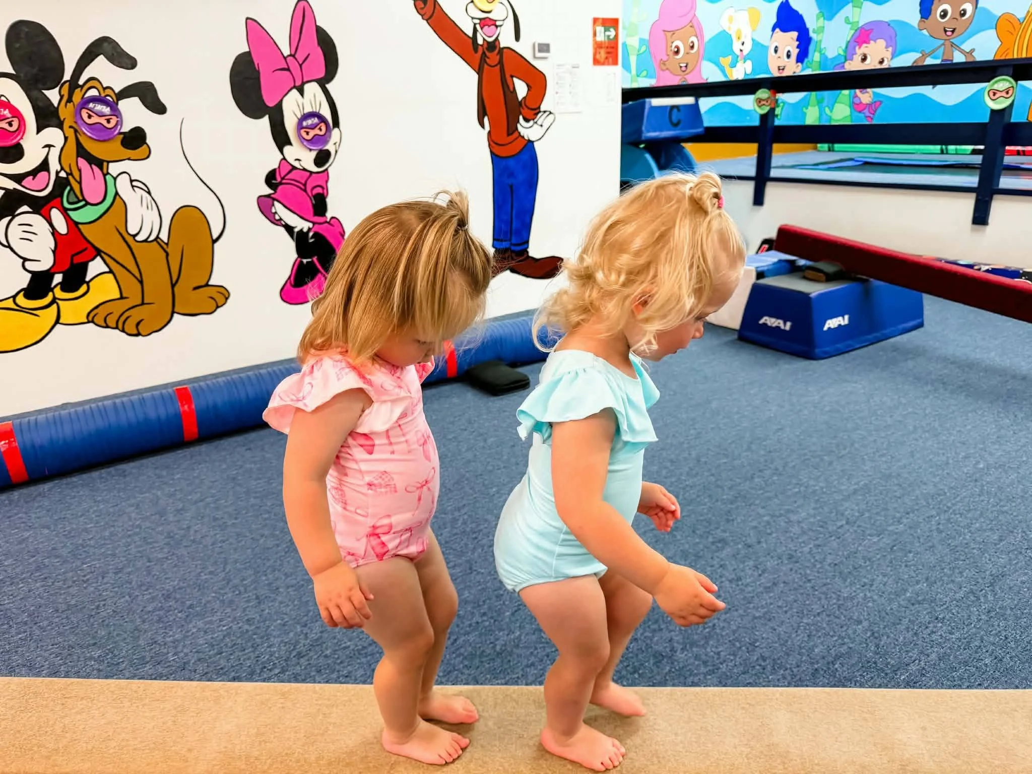 Two toddlers in leotards walking along a low beam in the Scamps preschool gym