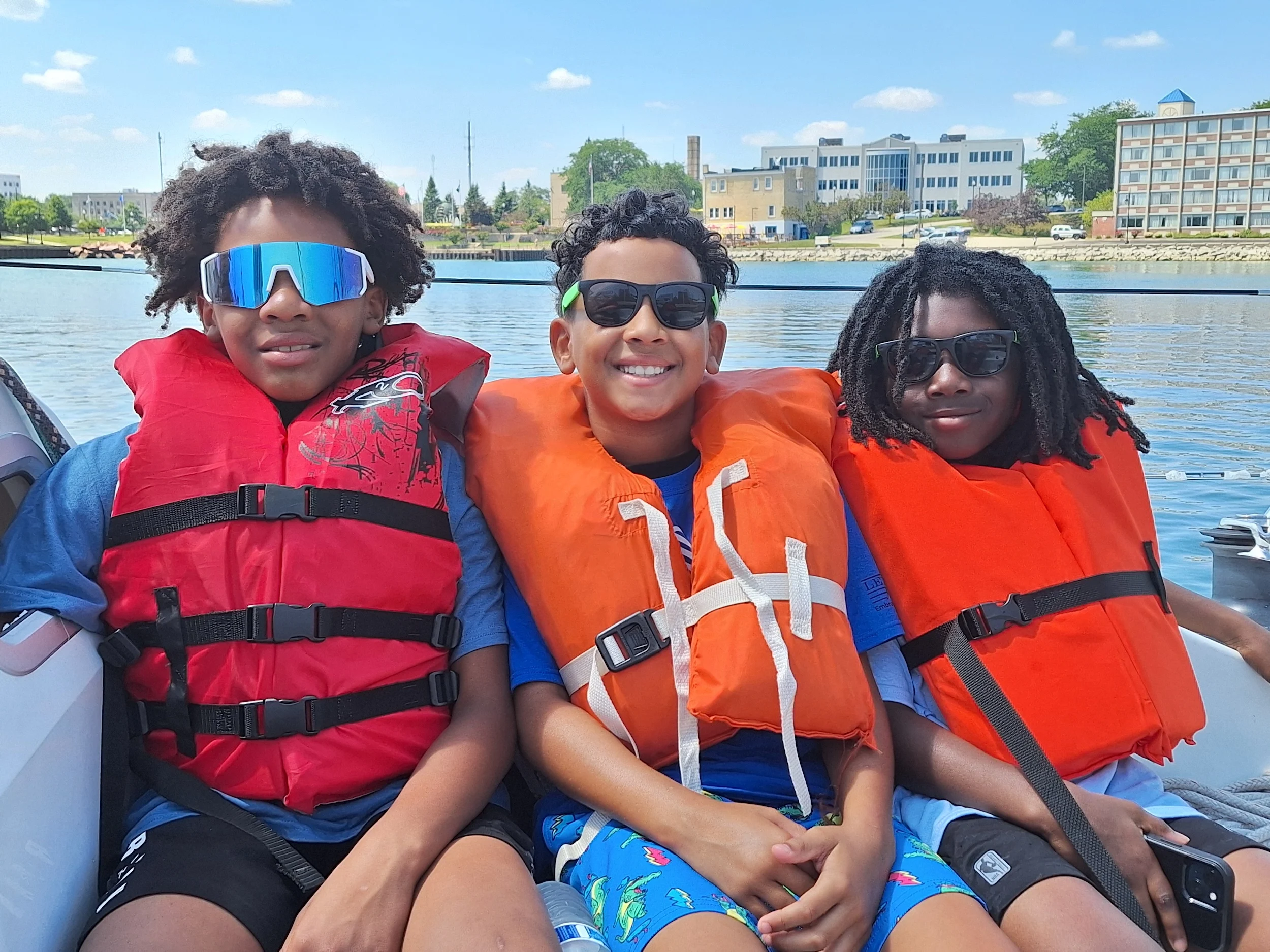 Three Club members in life jackets smiling on a summer boat ride