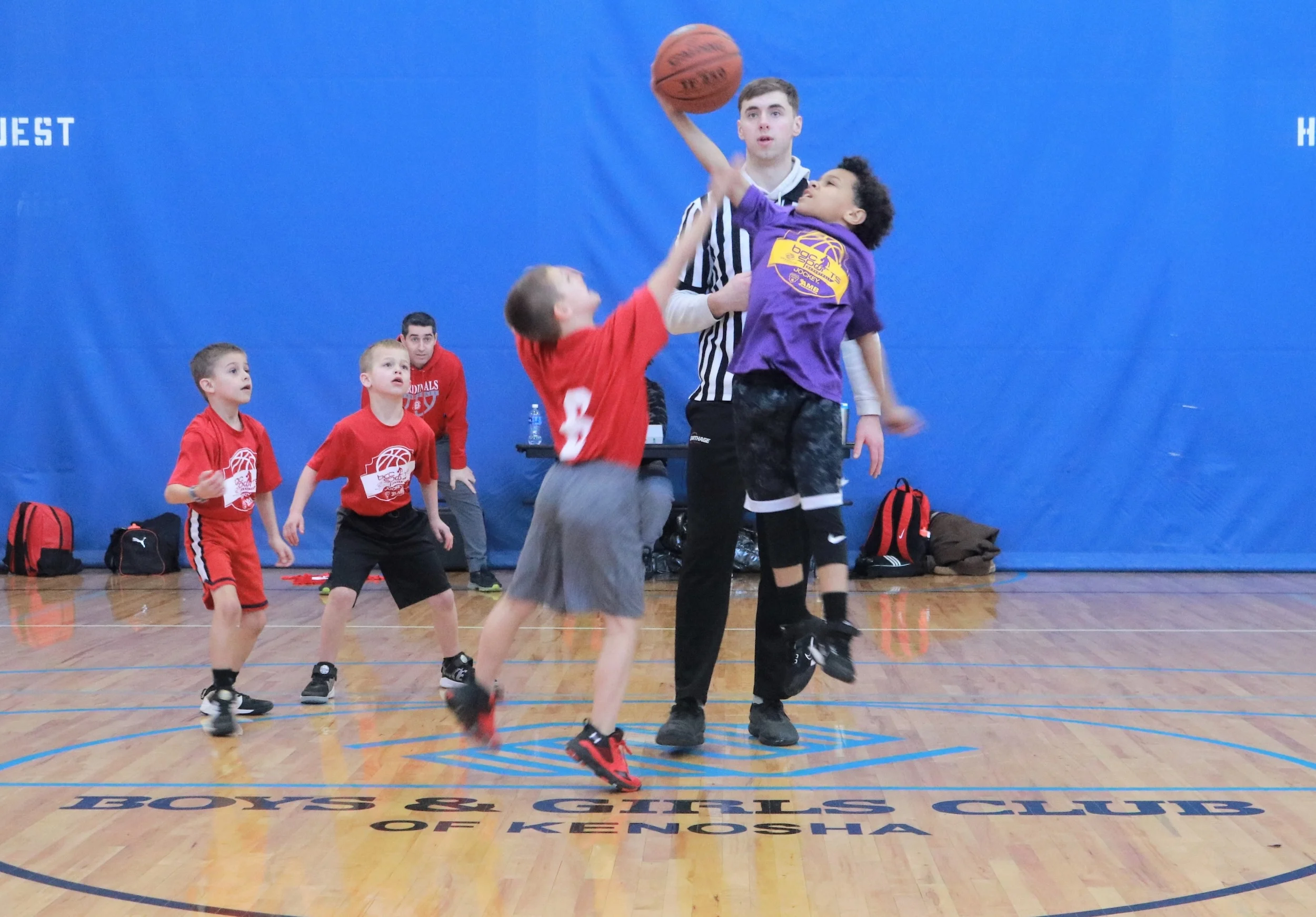 Referee tossing up the ball for a jump ball at a youth basketball game on the Club's court