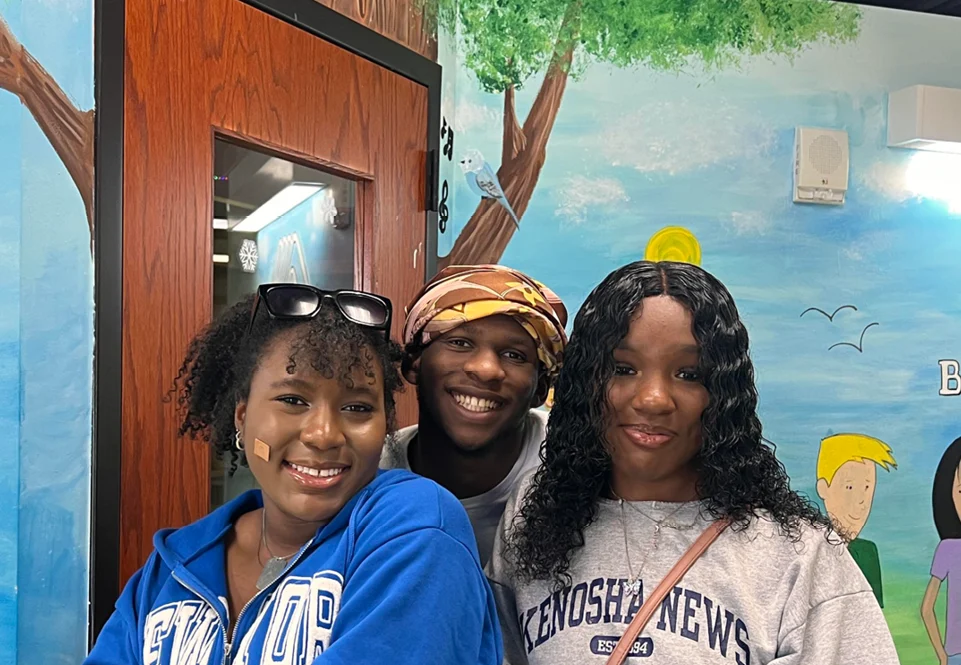 Three teens smiling together in front of a painted mural at the Club