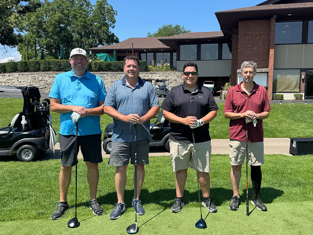 2026 Golf Outing4 Four golfers standing with their clubs beside the golf carts