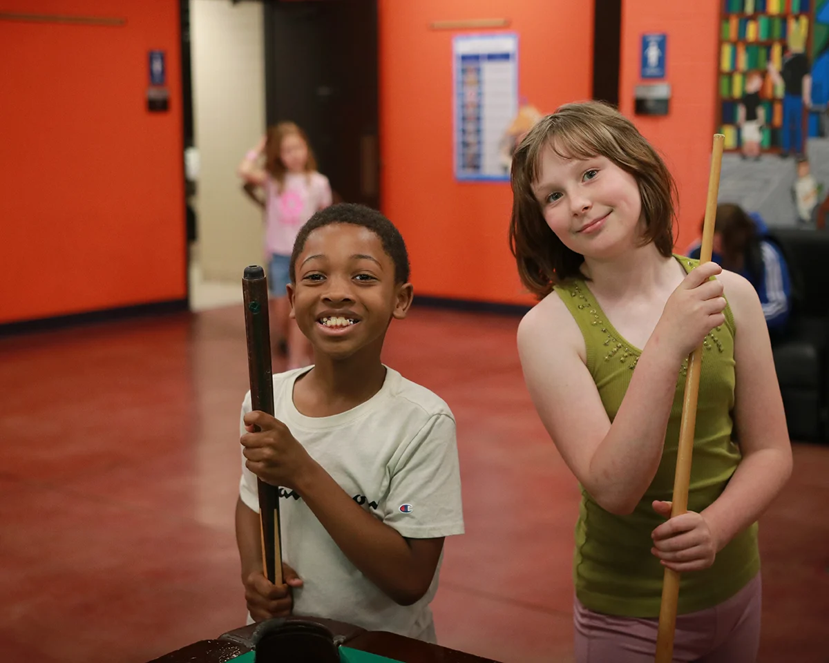 Two Club members smiling and holding pool cues in the game room