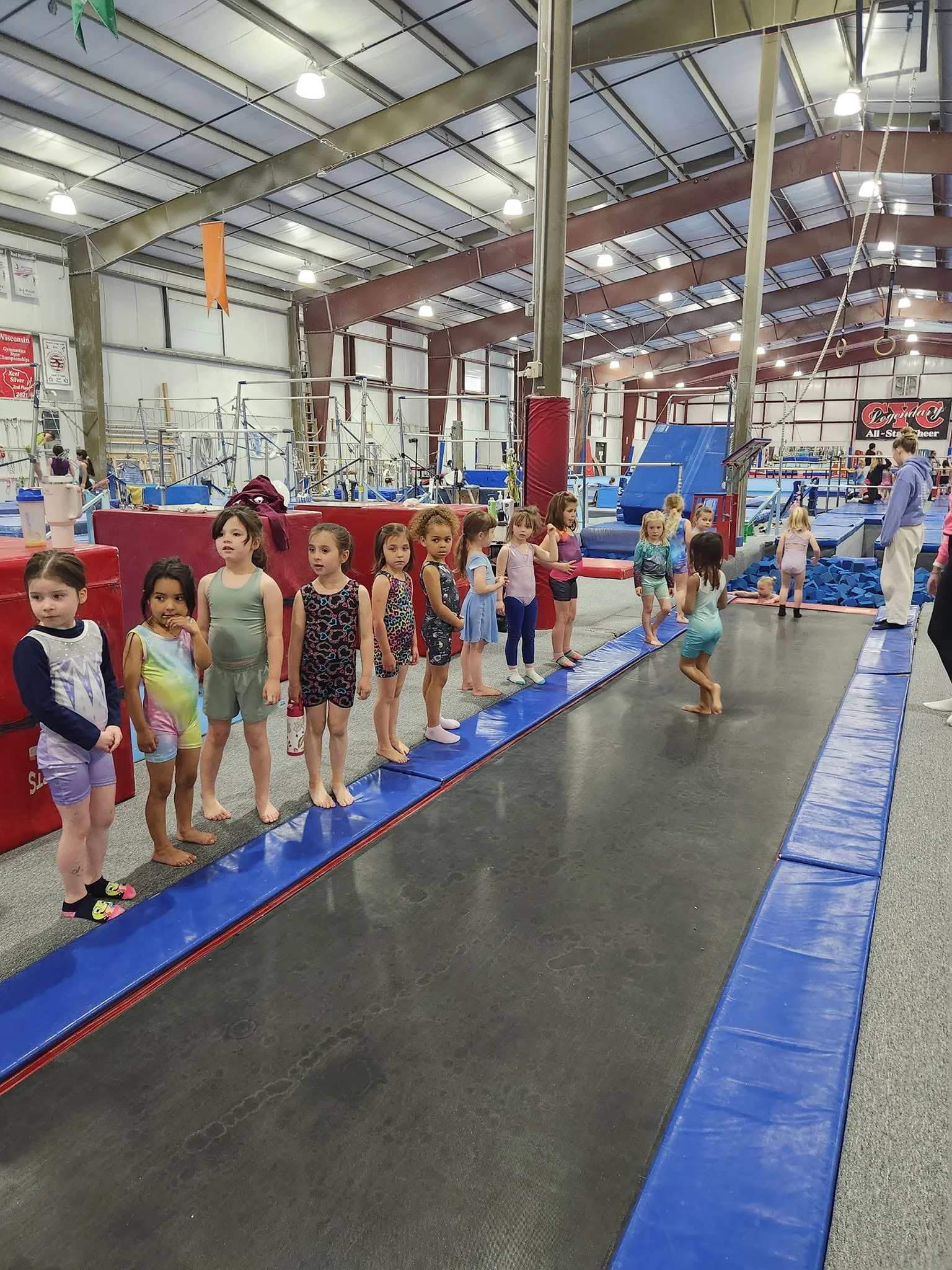 Gymnasts lined up at the tumble track during Tumbling & Trampoline practice at Scamps